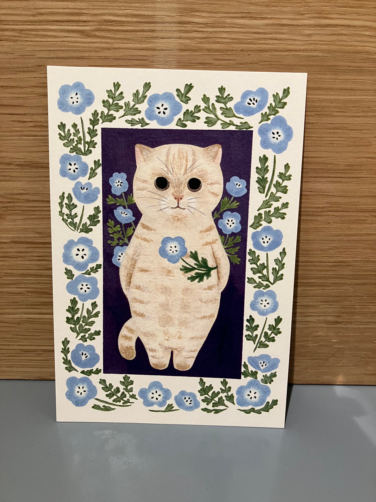 Japansk kort med lysegrå kat der holder lyseblå blomster