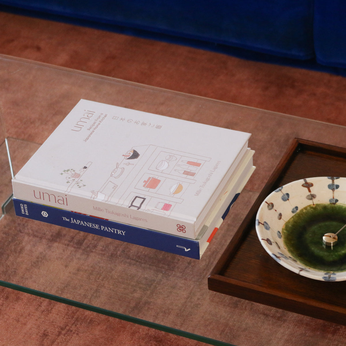 Japanske kogebog på et glasbord ved siden af en keramisk skål på en træbakke.