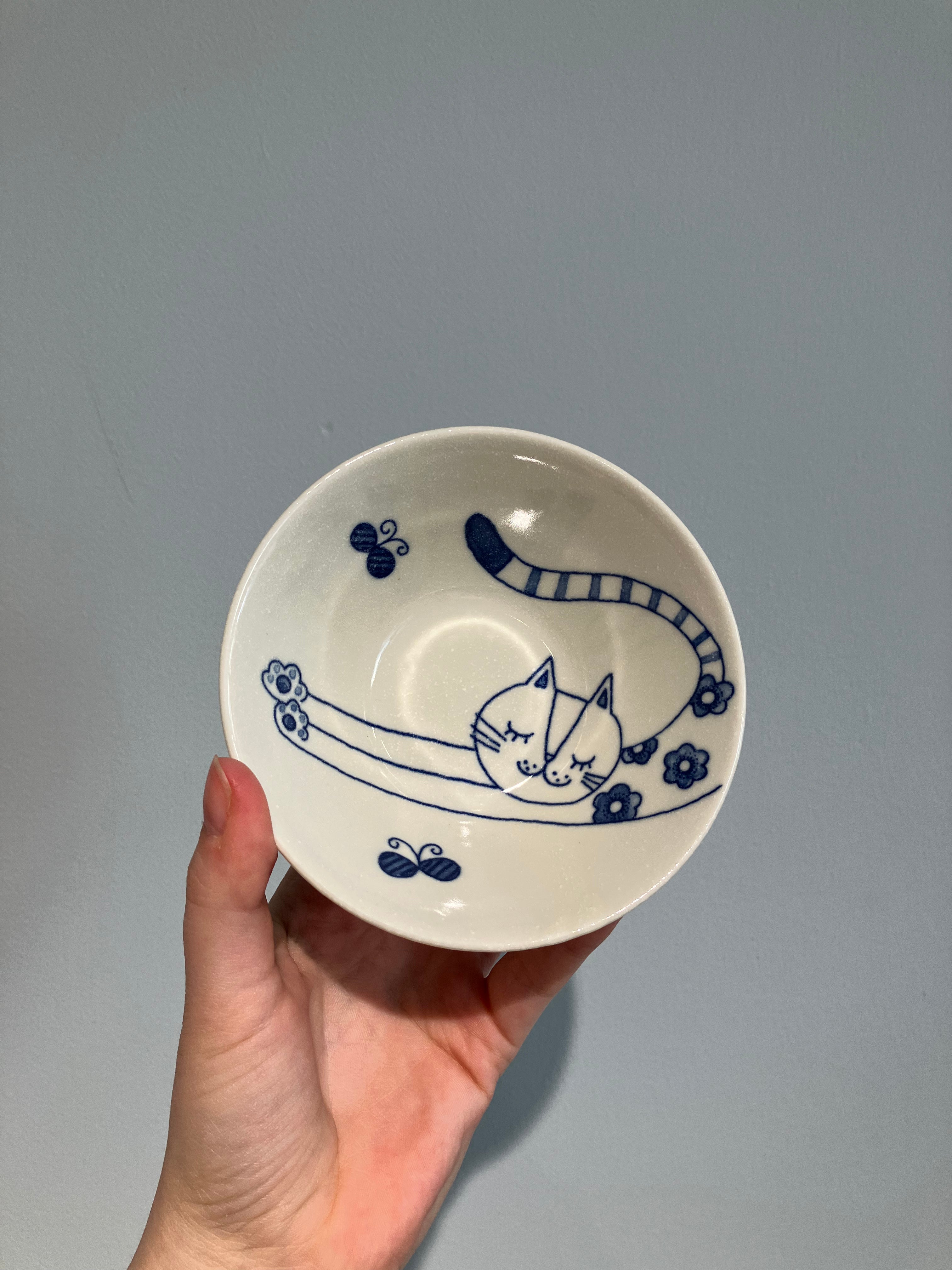 Small white bowl with blue cat stretching