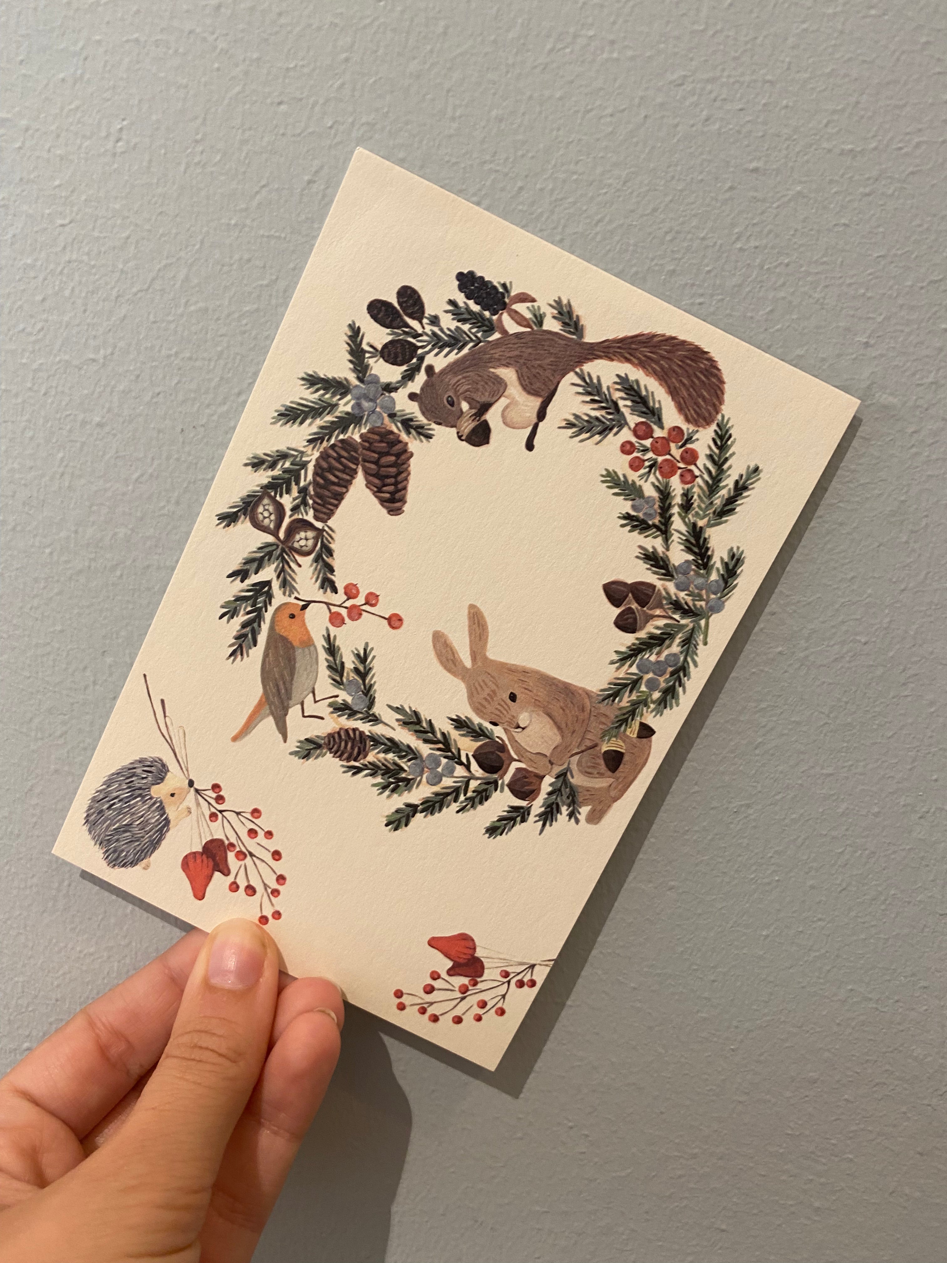 Postcard with forest animals and wreath of spruce and fir cones