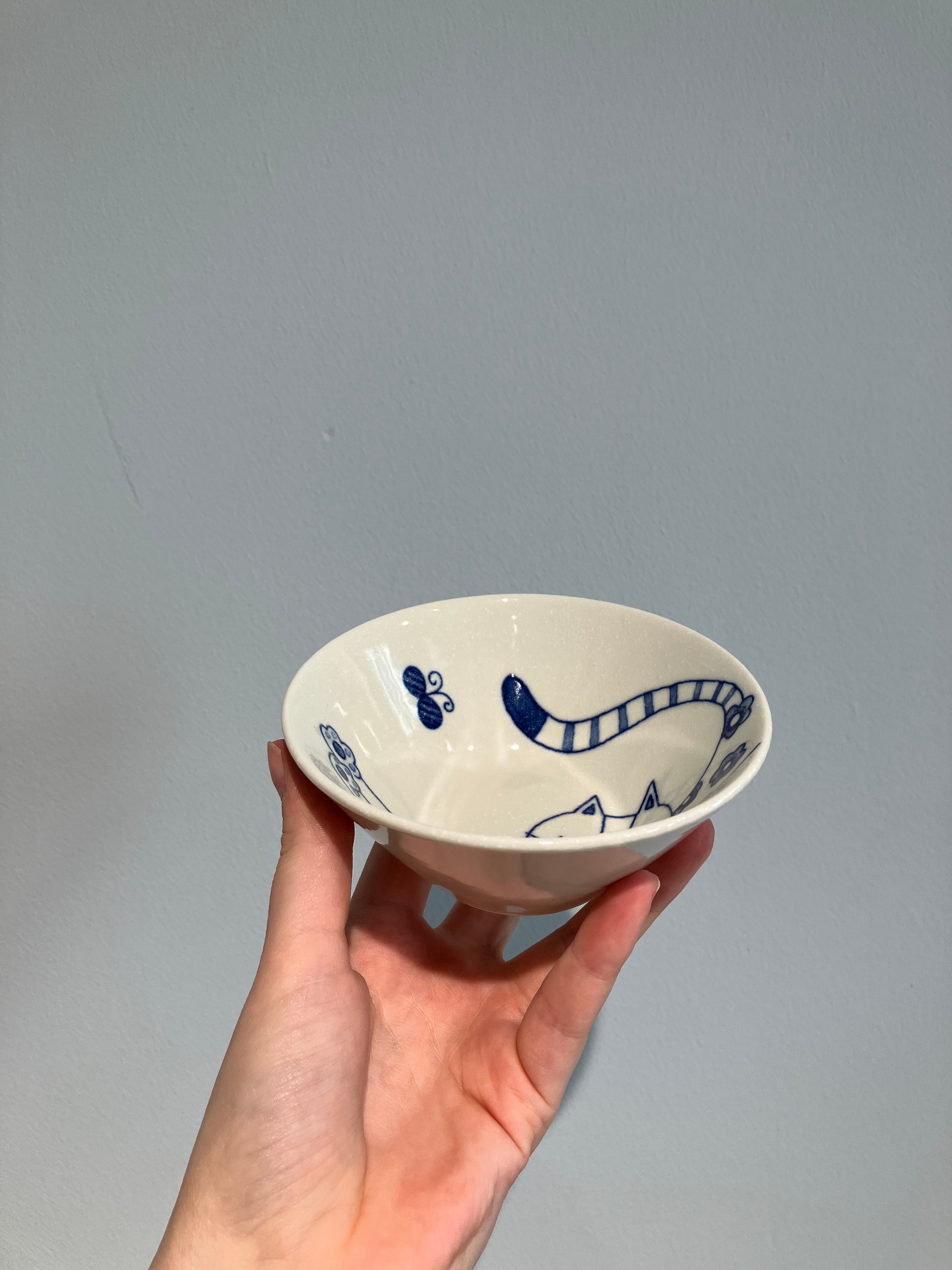 Small white bowl with blue cat stretching